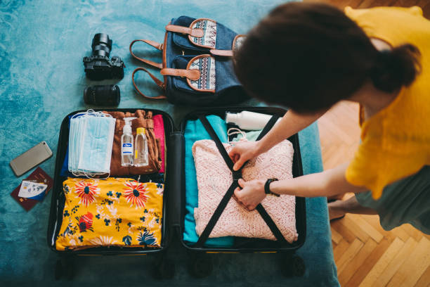 Woman packing suitcase for summer travel, including face masks and airplane travel-sized antibacterial hand gels