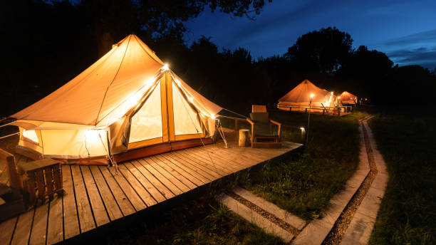 Tents with burning torches, lamps and wooden chairs at glamping, forest around, night