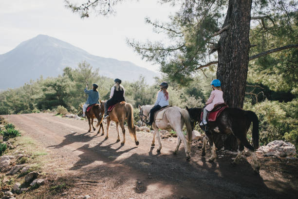 A young woman takes photos of a group of people on her smartphone  riding a horse through picturesque landscapes.
