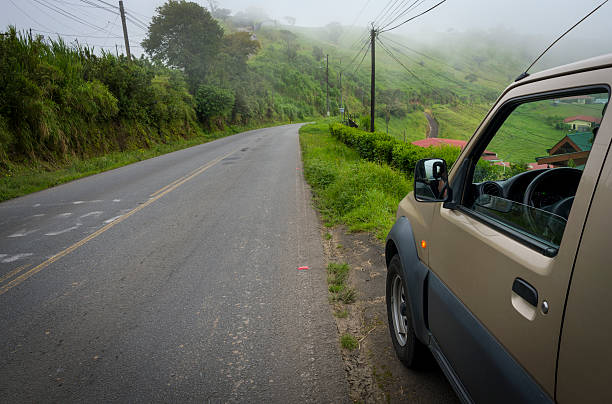 Car parked in the side of a road in the Costa Rica countryside during a fogy morning.