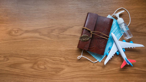 Top view of notebook,toy plane,hand sanitizer and face mask on a wooden background with copy space.Covid-19 and travel concept.