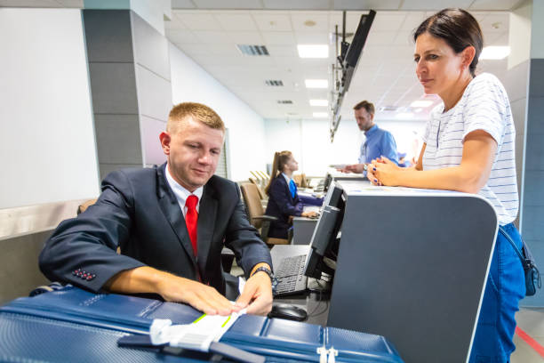 Male airline attendant doing check-in and attaching tag on passenger luggage. Woman waiting at the check-in counter.