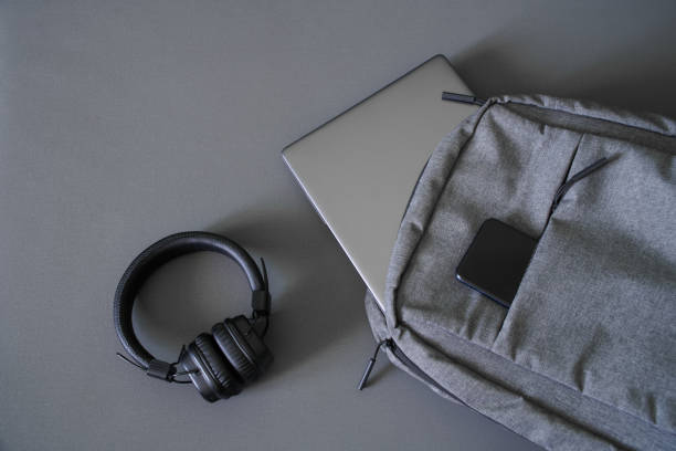 A small textile urban backpack with a steel-colored laptop or ultrabook, a smartphone and wireless headphones. Traveling with gadgets. Hand luggage at the airport. Close-up