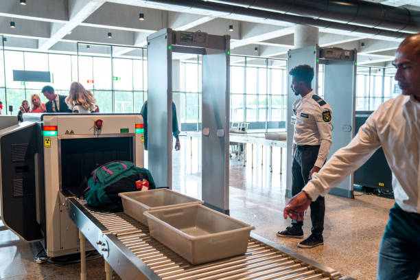 Partial shot of a mid adult South American man reclaiming his hand luggage after the x-ray machine. Metal detector door and an African security officer in the background.